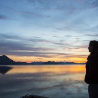 Student looking out onto a sunset over the water at the Alaska Salmon Camps