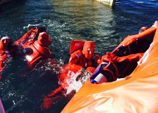 Students wearing survival suits climb into a covered life raft during a drill.