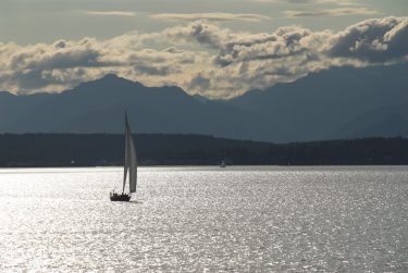 Sail boat in Puget Sound waters with mountains in the background.