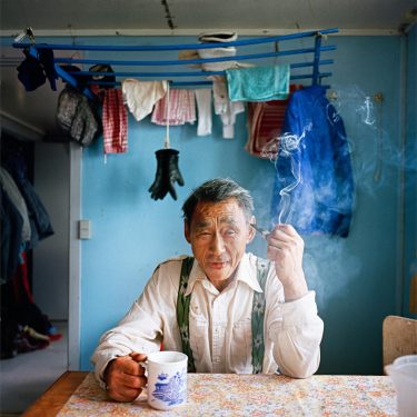 Older man sitting at kitchen table with a coffee mug and cigarette.