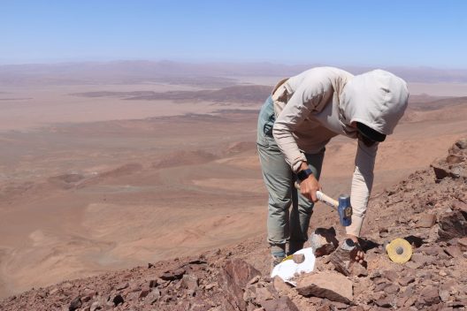 UW doctoral student collects rock samples on dry, brown hills in Chile’s Atacama Desert.